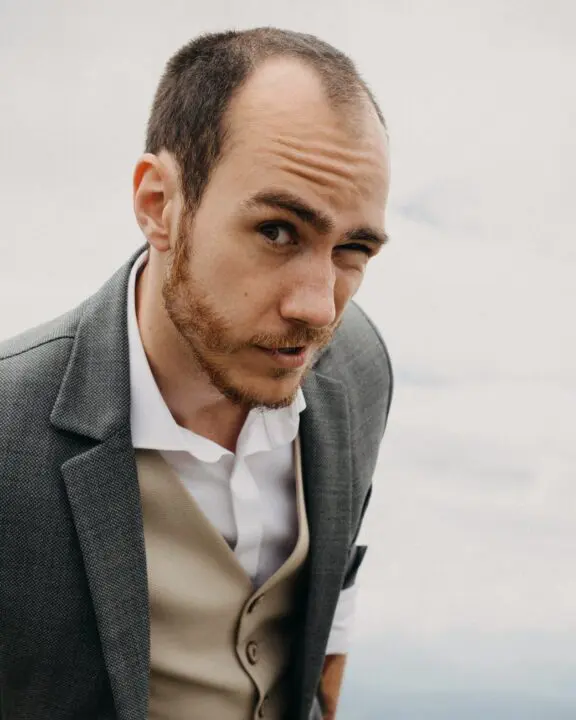 stylish man squinting eye against cloudy sky
